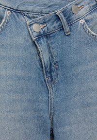 Jean en denim bleu vu de face montrant la fermeture éclair, deux boutons en métal, une passants de ceinture et les bords de poches cousus.