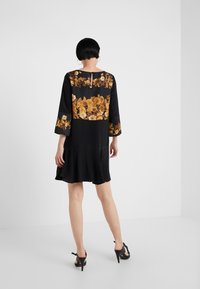 Vestido negro con mangas tres cuartos y un respaldo con patrón floral. Presenta un escote redondo y un dobladillo acampanado, hecho de una tela suave.