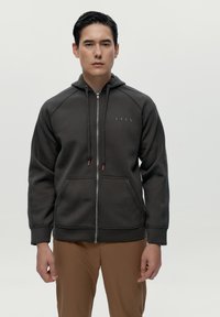 Tmavošedá mikina na zips s predným vreckom, nastaviteľnou kapucňou so šnúrkou a tónovým logom na hrudi; hladký materiál s rebrovanými manžetami.