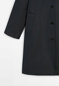 Zwarte trenchcoat met een rechte snit, gemaakt van gladde stof. Bevat vijf knopen, een zijzak en een kraag met een nette afwerking.