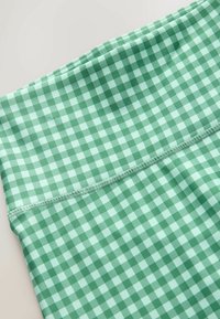 Közeli kép világos és sötétzöld kockás anyagról, ahol látható a varrás egy varrat mentén.