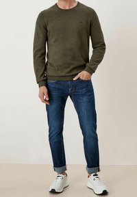 Pull en tricot vert olive avec un col rond, associé à un jean en denim bleu avec revers et des baskets blanches. Design simple sans motifs.