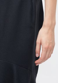 Right hand relaxed beside black textured fabric dress or garment on light background.