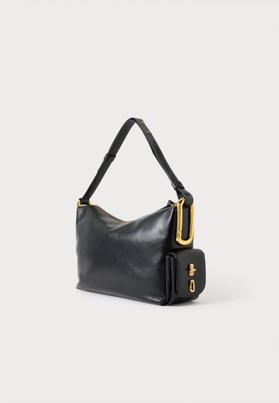 Sac à bandoulière en cuir noir avec sangle réglable, ferrures dorées et petite poche avant avec fermeture à boucle sur fond blanc.