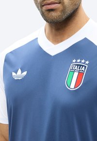 Mann trägt blau-weißes Italien-Trikot mit Adidas-Logo und vier Sternen als Nationalmannschafts-Emblem auf der Brust.