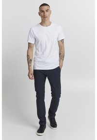 Vit bomullströja med korta ärmar, kombinerad med marinblå byxor och svarta sneakers. Enkel design utan mönster eller synlig hårdvara.