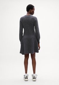 Abito grigio a maglia con maniche lunghe, orlo svasato, scollatura rotonda e finitura testurizzata, abbinato a scarpe da ginnastica bianche e nere.