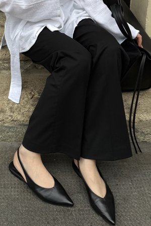 Svarta läder slingback-tofflor med spetsiga tår, slät textur och minimalistisch design, kombinerat med svarta vida byxor och en vit topp.