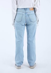 Jeans de tiro alto en azul claro, con pierna recta, diseño de cinco bolsillos, etiqueta en el parche trasero y un desgaste mínimo. Acompañados de zapatillas grises.