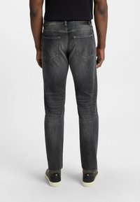 Jeans neri con vestibilità slim, caratterizzati da una texture scolorita, cuciture rinforzate e due tasche posteriori. Indossati con sneaker nere e bianche.