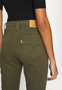 Olivgröna hög midja jeans med en slät yta, bakfickor med rundad sömnad och en beige Levi's-lapp på midjebandet.