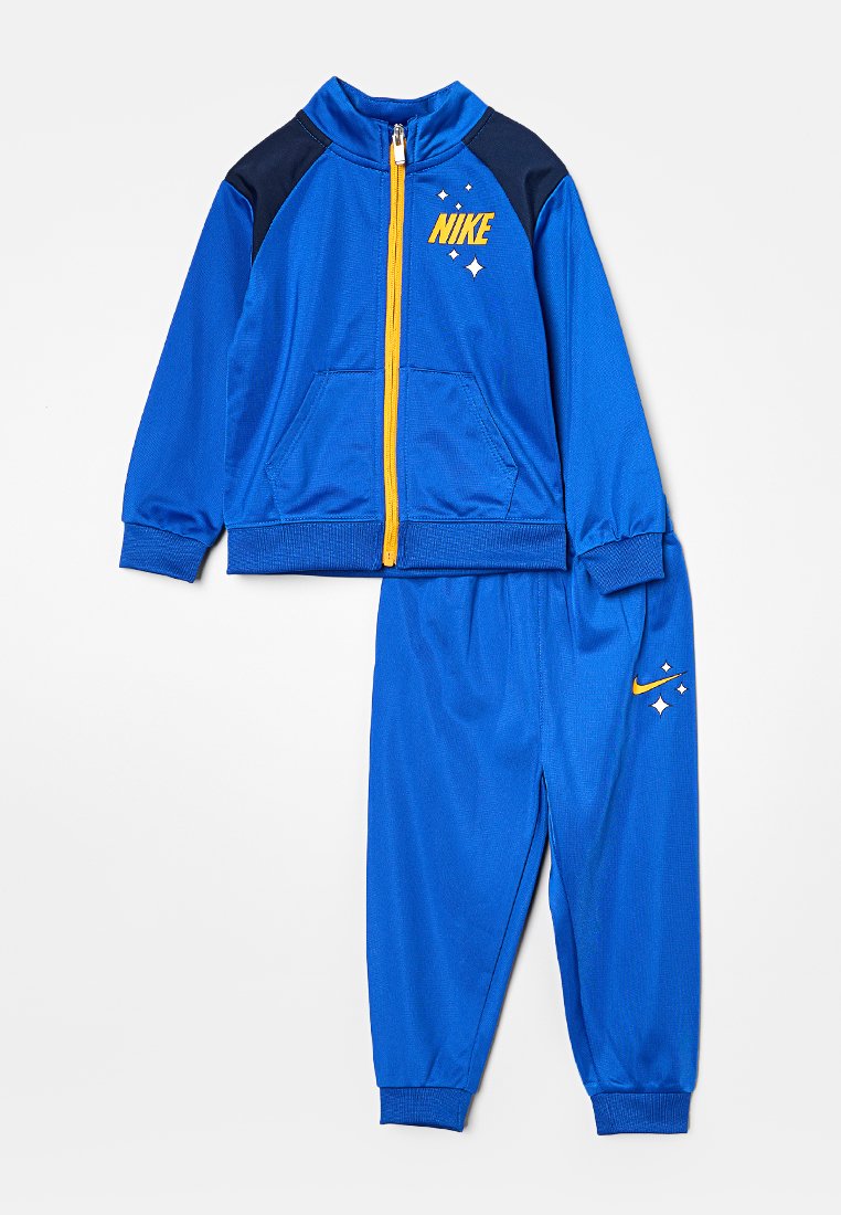 Tuta Nike blu con giacca con zip caratterizzata da accenti gialli e spalle nere; pantaloni abbinati con logo e dettaglio stelle.