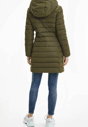 Oliwkowo-zielony pikowany płaszcz z kapturem, z pikowanym wzorem, długimi rękawami i długością do połowy uda, zestawiony z niebieskimi dżinsami i białymi trampkami.