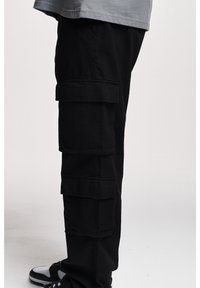 Mustat cargo-housut, joissa on useita paikkataskuja ja jotka on valmistettu teksturoidusta kankaasta. Mallissa on suorat lahkeet ja se istuu mukavasti vyötärölle.