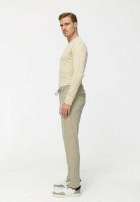 Beige hosszú ujjú ing, világosszürke mintás nadrággal párosítva. A modellen fehér sportcipők vannak, szürke és fekete akcentussal.