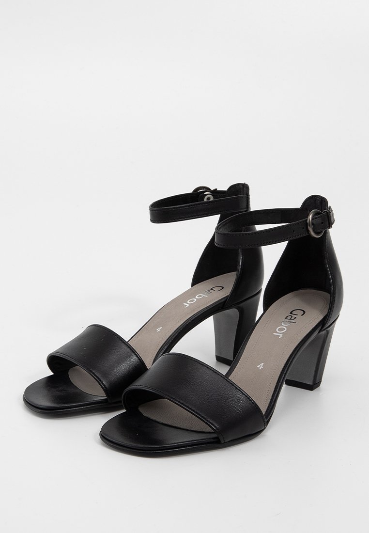 Sandales ouvertes en cuir noir avec une large bride avant, une bride de cheville et un talon épais. Texture lisse avec un design minimaliste.