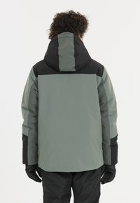 Isoleret jakke i grøn og sort, med hætte, tekstureret stof og lange ærmer. Bagsiden har et farveblokdesign og elastiske manchetter.