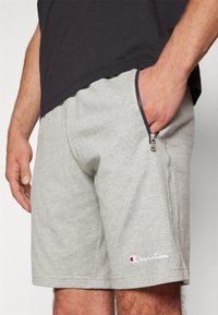 Pantalones cortos de algodón grises con cremallera lateral, que cuentan con un logotipo bordado. El material tiene una textura suave y un diseño casual.