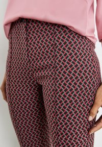 Pantaloni neri con un motivo geometrico rosso e grigio. Presentano una texture liscia e un design aderente, parzialmente coperti da una maglietta rosa.