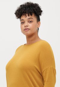 Mustard yellow, long-sleeve top with a loose fit, round neckline, soft texture, and dropped shoulder seams. Simple and casual design.