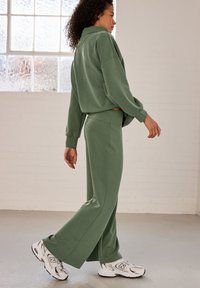 Green cotton sweatshirt and matching wide-leg pants, both featuring a relaxed fit and soft texture, paired with white sneakers.