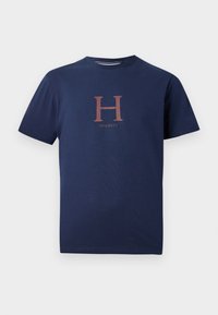 Tmavomodré bavlnené tričko s veľkým, kontrastným medeným písmenom "H" a slovom "Hacket" nižšie v jednoduchom, modernom serifovom písmene.