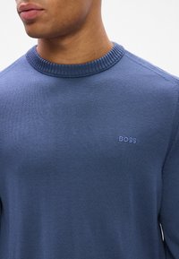 Men's blue knit sweater featuring a ribbed collar and small embroidered "BOSS" logo on the chest. Smooth texture, fitted design.
