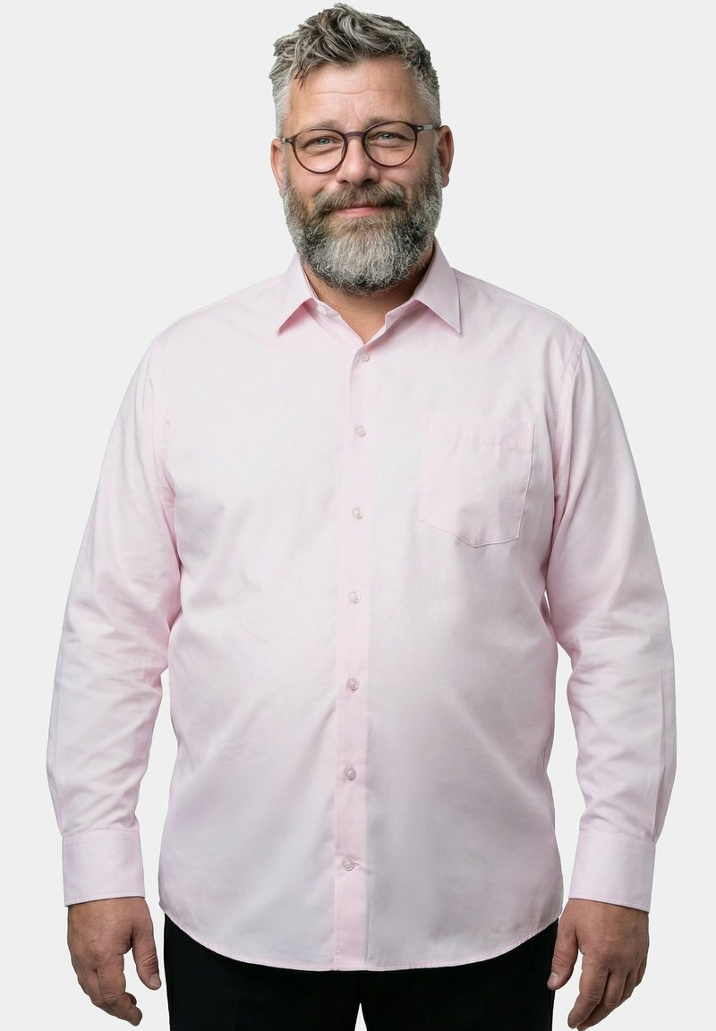 Mann mittleren Alters mit grauem Bart und Brille, der ein hellrosa Hemd mit Knöpfen trägt und vor einem schlichten Hintergrund lächelt.