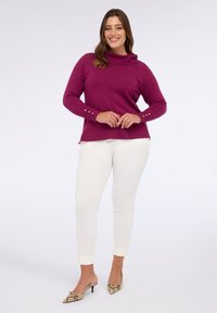 Jersey morado con cuello cisne y mangas largas, adornado con botones dorados, combinado con pantalones ajustados blancos y tacones con estampado de serpiente.