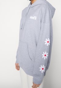 Sudadera gris de mezcla de algodón, con un bolsillo frontal, capucha con cordón y margaritas blancas con centros rojos en las mangas.