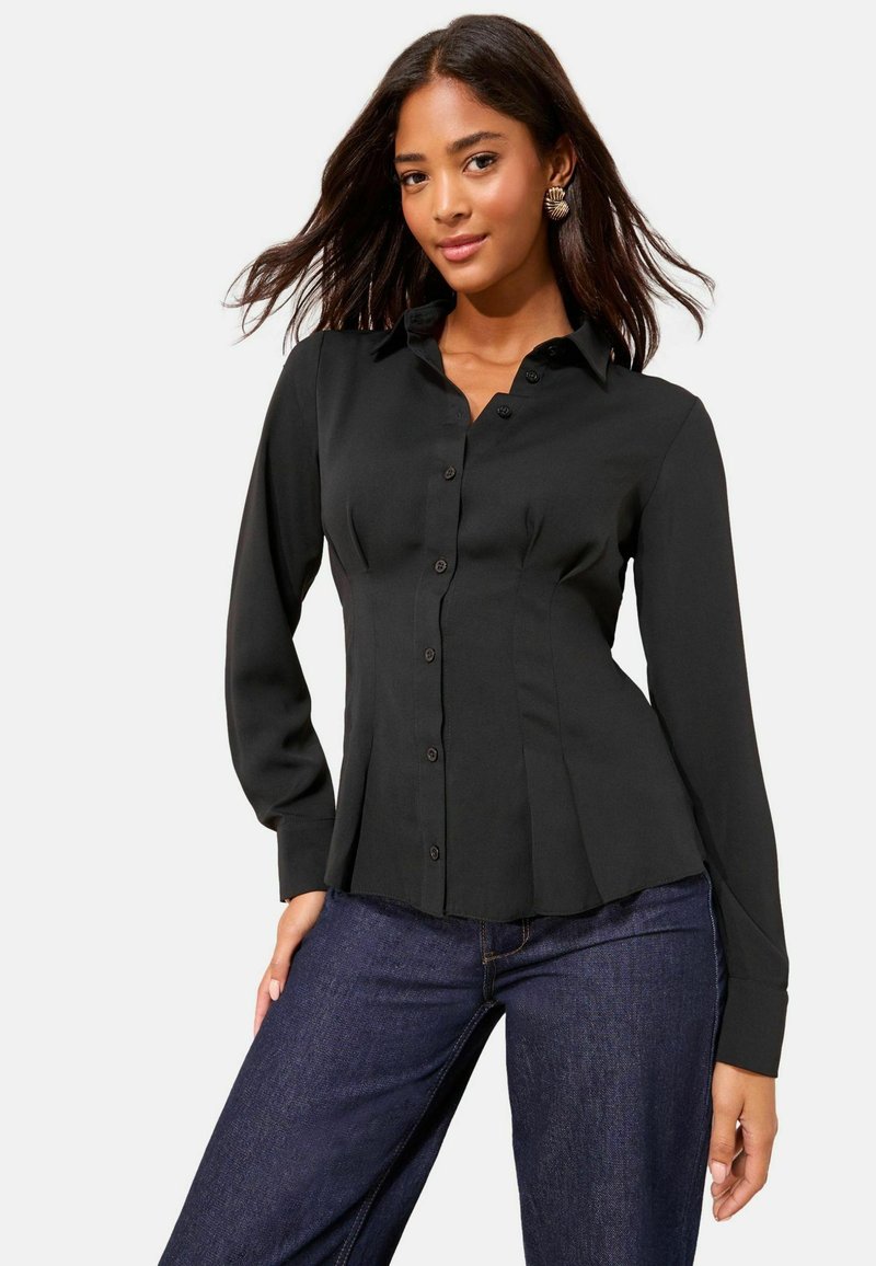 Juodas marškinis su struktūruotu dizainu, ilgomis rankovėmis ir raukšlėmis ties juosmeniu. Pagamintas iš lygios medžiagos, tinkamas tiek kasdieniam, tiek oficialiam dėvėjimui.