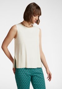 Top senza maniche di colore crema con pieghe laterali, abbinato a pantaloni color teal con un motivo geometrico. Tessuto liscio e vestibilità rilassata.