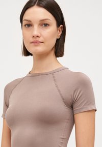 Fitted, short-sleeve top in light brown, made from smooth, stretchy fabric with visible seam detailing and a round neckline.