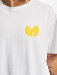 Witte katoenen t-shirt met een geel logo op de linkerkant van de borst. Ronde halslijn en korte mouwen. Gladde textuur.