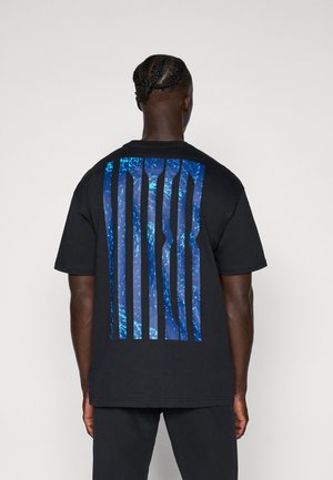 T-shirt noir avec un grand design graphique bleu et des lignes verticales au dos. Manches courtes et coupe décontractée. Matériau en coton.