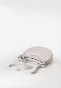 Borsa a tracolla in pelle grigia chiara con forma circolare, chiusura con zip e tracolla piatta. Texture liscia e design minimalista.