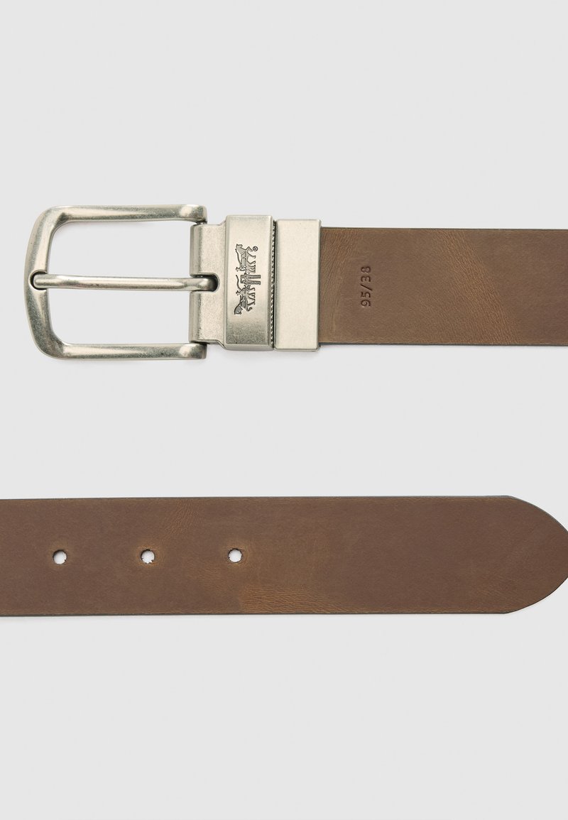 Brun læderbælte med en sølvmetal spænde, der har fem huller, en glat tekstur og afrundet spids. Logoet er præget på spænde.