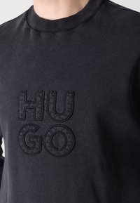 Sudadera negra con cuello redondo acanalado y un logo bordado elevado "HUGO" en la parte delantera, confeccionada en suave material de algodón.