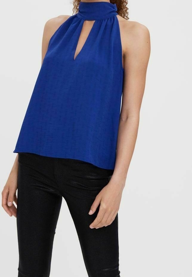 Femme portant un haut bleu sans manches à col licou avec une encolure en forme de trou de serrure, associé à un pantalon noir moulant sur un fond uni.