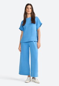 Top oversized di un blu chiaro con maniche corte abbinato a pantaloni larghi coordinati; tessuto morbido, cuciture minimal, vestibilità rilassata e orli a coste.