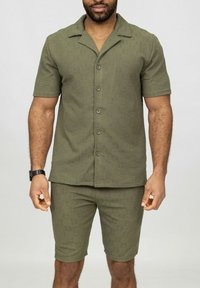 Chemise à manches courtes olive avec un col plat, en tissu texturé, associée à un short assorti, les deux présentant un motif subtil.