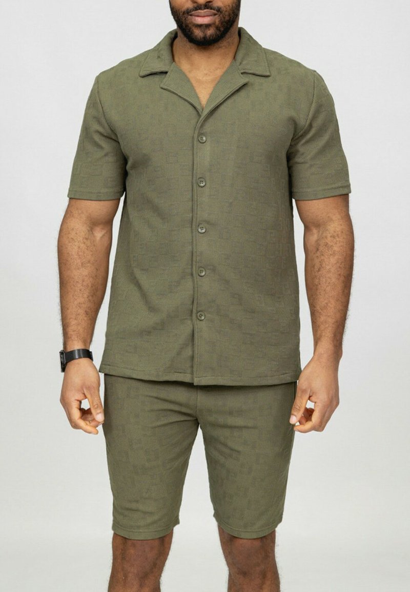 Chemise à manches courtes olive avec un col plat, en tissu texturé, associée à un short assorti, les deux présentant un motif subtil.