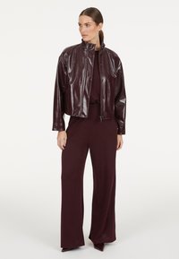 Burgundy cropped jacket in shiny synthetic material paired with a matching loose-fitting jumpsuit, showcasing a sleek, modern design.