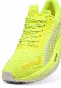 Scarpa da ginnastica gialla brillante con tomaia in mesh traspirante, sistema di allacciatura prominente, accenti riflettenti e suola in schiuma leggera.
