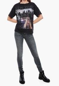Camiseta gráfica negra con el horizonte de Nueva York y la Estatua de la Libertad. Combinada con jeans ajustados grises y botines negros.