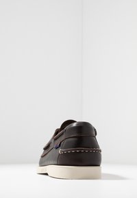 Dunkelbraunes Leder-Schuhwerk mit hellfarbener Sohle, mit einem Schlupfdesign und kontrastierenden Nähten. Ikonisches Logo-Tag an der Seite.