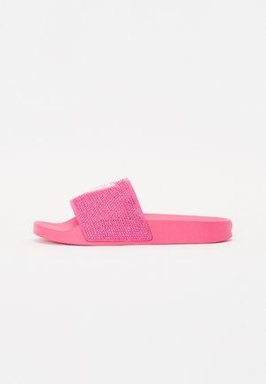 Des sandales à talons plats roses avec une tige texturée et ornée de strass, et une semelle en caoutchouc. La forme générale est ouverte à l'avant avec une large bride.