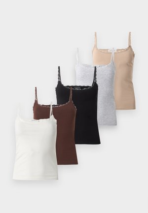 Femme portant des lunettes de soleil noires, un haut sans manches noir, un jean bleu ample et des sandales compensées noires, debout les mains dans les poches.