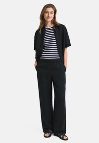 Maglietta nera a maniche corte sopra una maglietta a righe blu navy e bianca. Pantaloni neri larghi con elastico in vita e sandali.