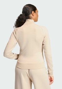 Chaqueta beige con cremallera, cuello alto, textura suave y diseño ajustado. Cuenta con puños y cinturilla acanalados. Vista trasera mostrada.